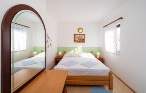 A bedroom with a wooden bed, a bedside table, a mirror, a clock, and a window with curtains. - Beach front apartment in Rovanjska (Rovanjska)