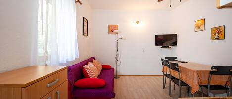 A compact living space with a sofa, a dining table, a TV, and a ceiling fan.