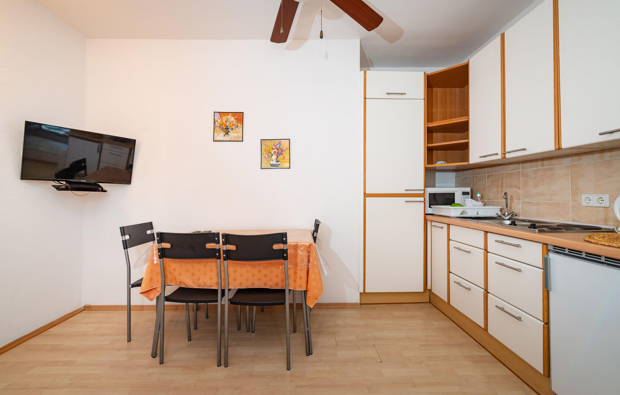 A compact kitchen with white cabinets, a microwave, and a sink. There is a dining table with chairs and two framed pictures on the wall.