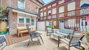 A patio with a wooden table and chairs, a metal folding chair, and a brick wall with decorative elements. - Awesome home in Arques la Bataille (Arques la Bataille)