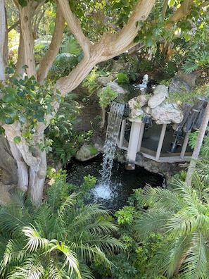 A waterfall cascading into a pond surrounded by lush greenery and a large tree. - BeachFRONT Condo E-18 on the H20! Oceanside, CA - North Coast Village. (Oceanside)