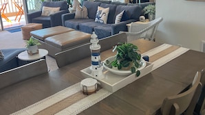 Ett modernt vardagsrum med en soffa, ett soffbord och ett matbord. Det finns växter, en liten modell av en fyr och en utsikt över havet genom stora fönster.