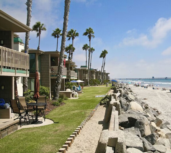 A beachfront hotel with multiple-story buildings, a grassy lawn, outdoor seating, and a rocky shoreline. - BeachFRONT Condo E-18 on the H20! Oceanside, CA - North Coast Village. (Oceanside)