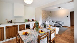 A modern kitchen with wooden cabinets, a dining table set with fruits and a bottle of wine, and a stone wall in the background. - 3 bedroom awesome home in Lamon (Lamon)