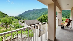 A balcony with a view of a mountainous landscape, a small building, and a chair with a floral cushion. - 3 bedroom awesome home in Lamon (Lamon)