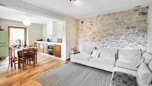 A modern kitchen with wooden cabinets, a dining area with a table and chairs, and a living room with a sofa and a stone wall. - 3 bedroom awesome home in Lamon (Lamon)
