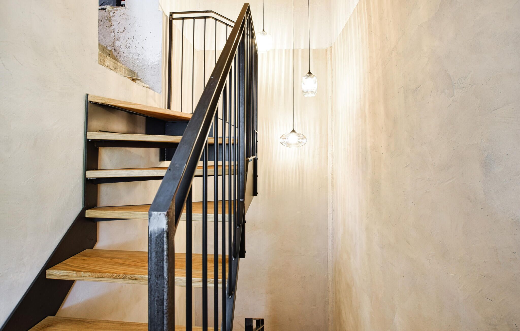 Una escalera de madera con barandilla de metal que sube a un piso superior.