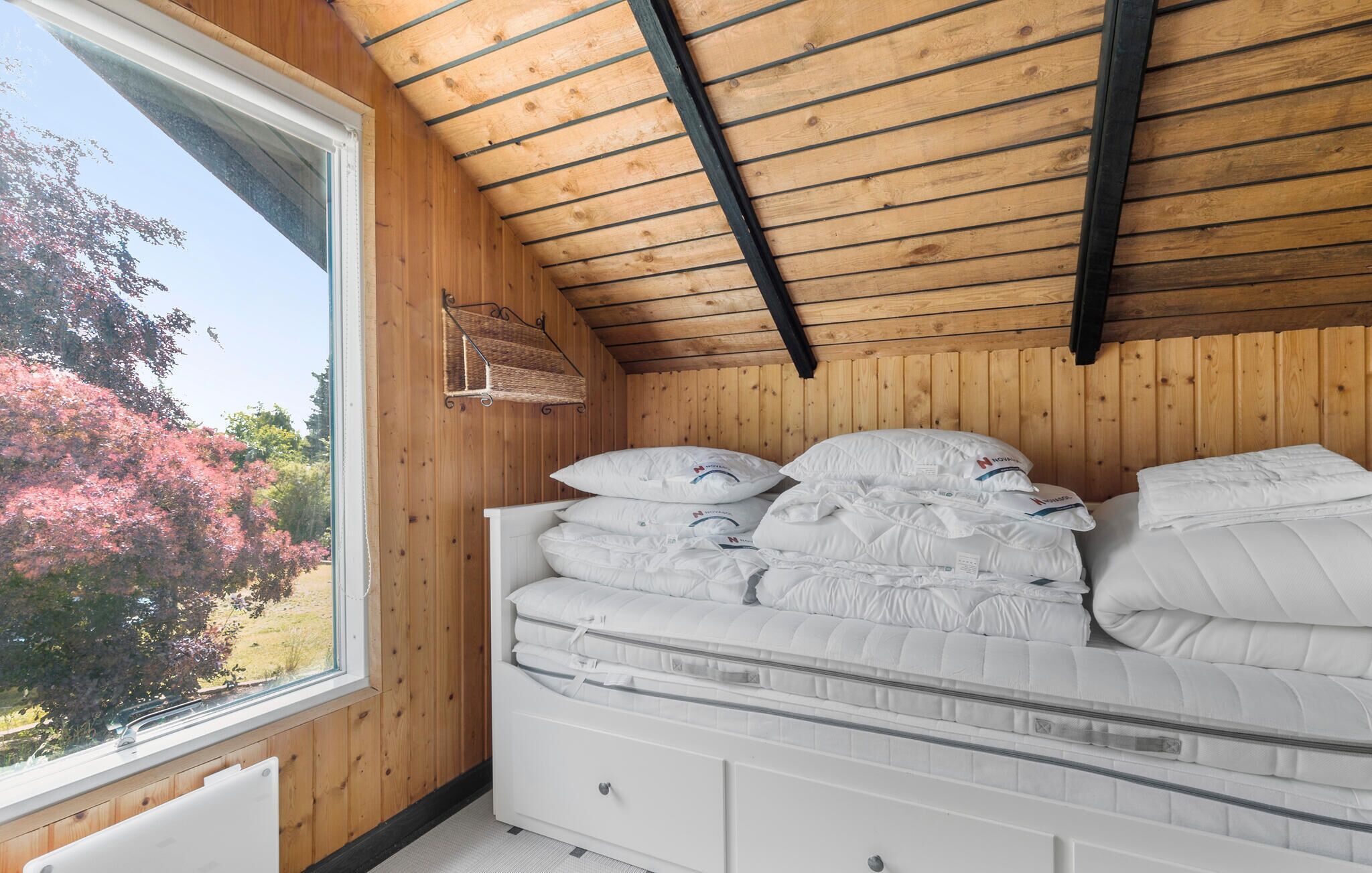 A bedroom with a wooden ceiling, a large window, and a bed with white bedding.