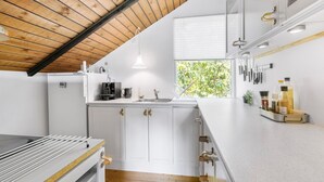 A modern kitchen with white cabinetry, a wooden ceiling, and a window providing natural light. - 2 bedroom lovely home in Melby (Melby)