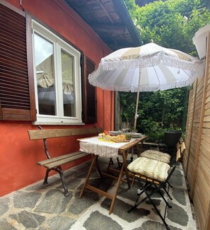 Une terrasse extérieure avec une table dressée pour les repas, un banc et un grand parasol.