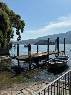A wooden dock with a boat, a stone pathway, and a clear view of a lake with mountains in the background.