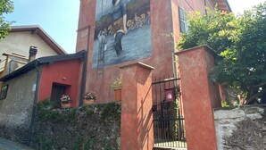 A building with a mural featuring a woman and musical instruments. - The Pink House of Riso Amaro In the painted village Legro  of Orta San Giulio (Orta San Giulio)