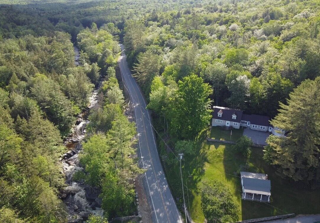 Vue aérienne d’une route traversant une zone boisée, avec une maison située sur le côté droit.