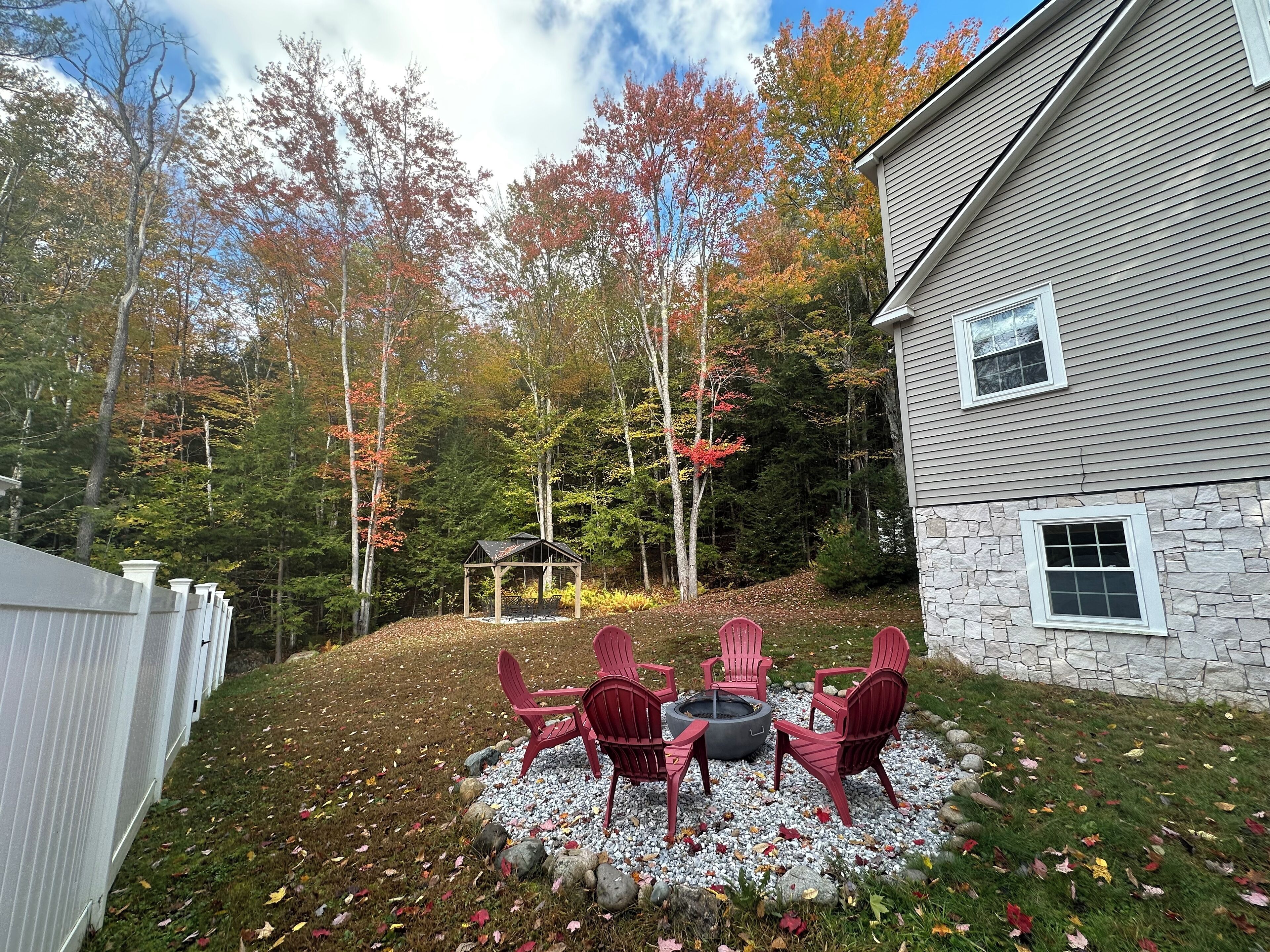 Un espace extérieur aménagé avec un mur en pierre, un foyer et des fauteuils Adirondack rouges.