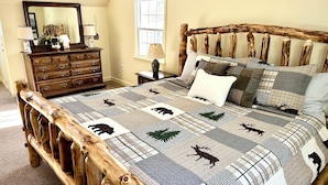 Quarto com estrutura de cama de madeira, colcha com estampas de animais, cômoda e espelho.