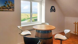 A room with a wooden barrel table, two chairs, a window with a view of the beach, and a wall clock. - Beautiful apartment in Kerlouan with WiFi (Kerlouan)