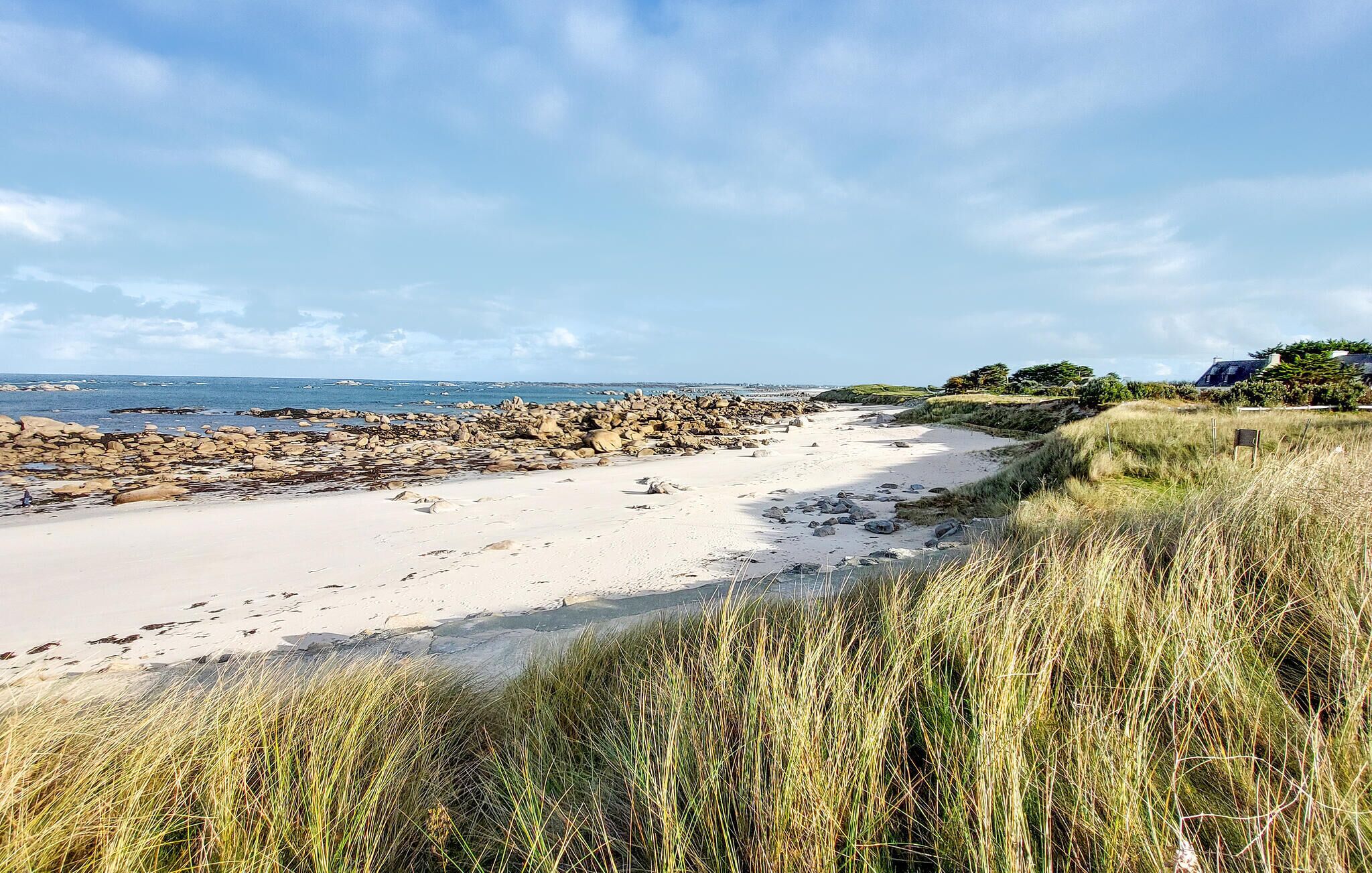 A coastal beach with rocky outcrops and grassy dunes.