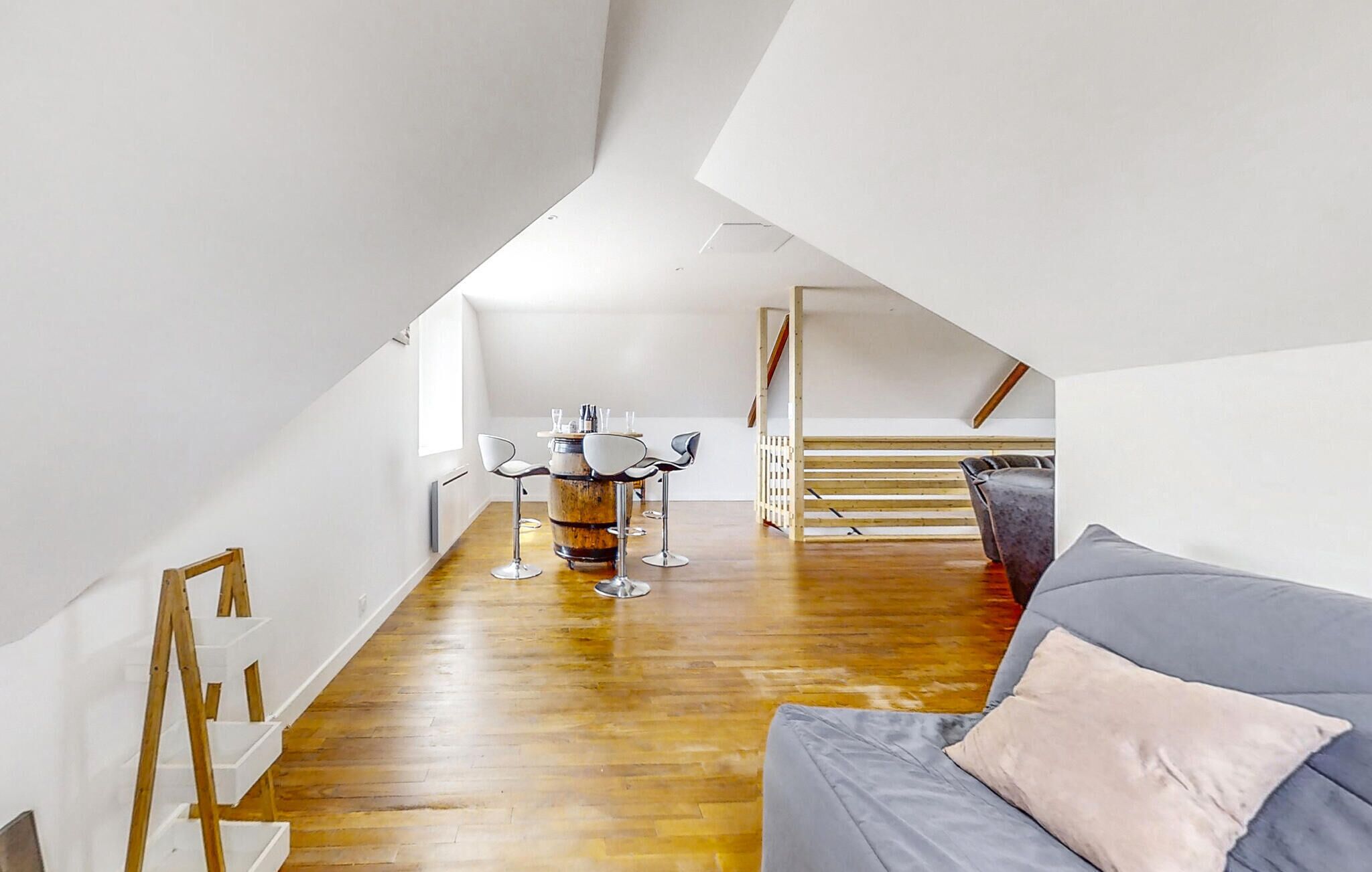 Ein modernes Loft mit Holzboden, einem grauen Sofa und einem Essbereich mit Tisch und Stühlen.