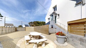 A modern house with a patio area featuring a stone table and benches, a wooden fence, and a potted plant. - Beautiful apartment in Kerlouan with WiFi (Kerlouan)