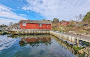 A red wooden boathouse with a dock extending into calm water, surrounded by rocks and sparse vegetation. - 4 bedroom lovely home in Fagerfjäll (Fagerfjäll)