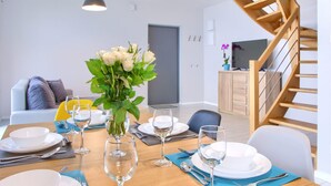 A dining area with a wooden table set for a meal, a vase of white flowers, and a staircase to the right.