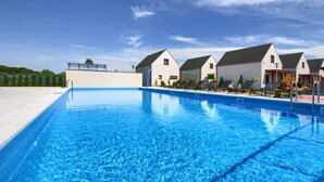 A swimming pool with lounge chairs and a building with a white facade and dark roofs.