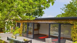 A modern outdoor dining area with a glass-enclosed patio, wooden furniture, and a view of the garden.
