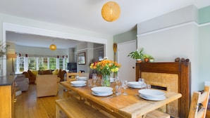 A dining area with a wooden table set for four, surrounded by wooden chairs. There is a vase with flowers on the table, and a wooden cabinet with decorative items on top.