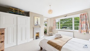 A bedroom with a bed, a dresser, a chair, a fireplace, and a window with curtains.