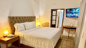 A neatly made bed with a headboard, a bedside table with a lamp, and a television mounted on the wall. - Room #1 two blocks from the Malecon (La Paz)