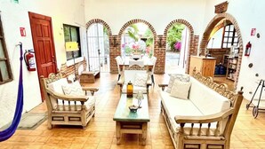 A cozy room with a sofa, two armchairs, and a coffee table. There is a fire extinguisher on the wall, a wooden door, and a window with a view of greenery. - Room #1 two blocks from the Malecon (La Paz)
