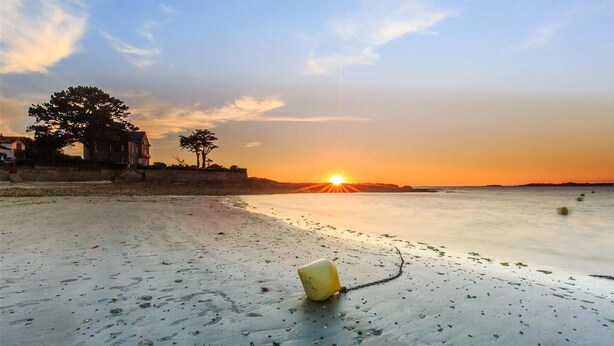 Ein Strand mit Sonnenuntergang, einem gelben Eimer und Fußabdrücken im Sand.