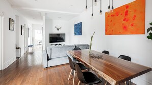 Un comedor moderno con una mesa de madera, sillas negras y un cuadro grande color naranja en la pared.