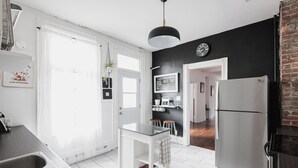 Una cocina moderna con encimera blanca, pileta de acero inoxidable y un reloj de pared negro.