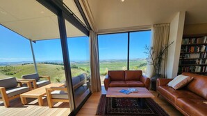 A spacious living area with a large window offering a view of the countryside. There are leather sofas, wooden furniture, and a bookshelf.