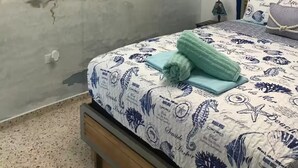 Une chambre à coucher avec une fresque murale sur le thème de la mer, un lit recouvert d’une couvre-lit à motifs nautiques et une tête de lit en bois.