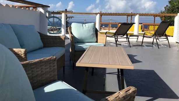 Un espace extérieur aménagé avec des meubles en osier et une table, offrant une vue sur une étendue d’eau.
