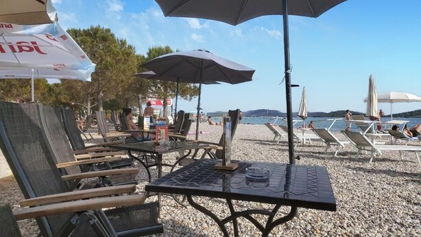 Outdoor seating with umbrellas, a table with a menu, and a view of the beach and water. - 3 bedroom lovely apartment in Vodice (Vodice)