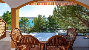 Un balcon doté de meubles en osier, offrant une vue panoramique sur la mer et la végétation.