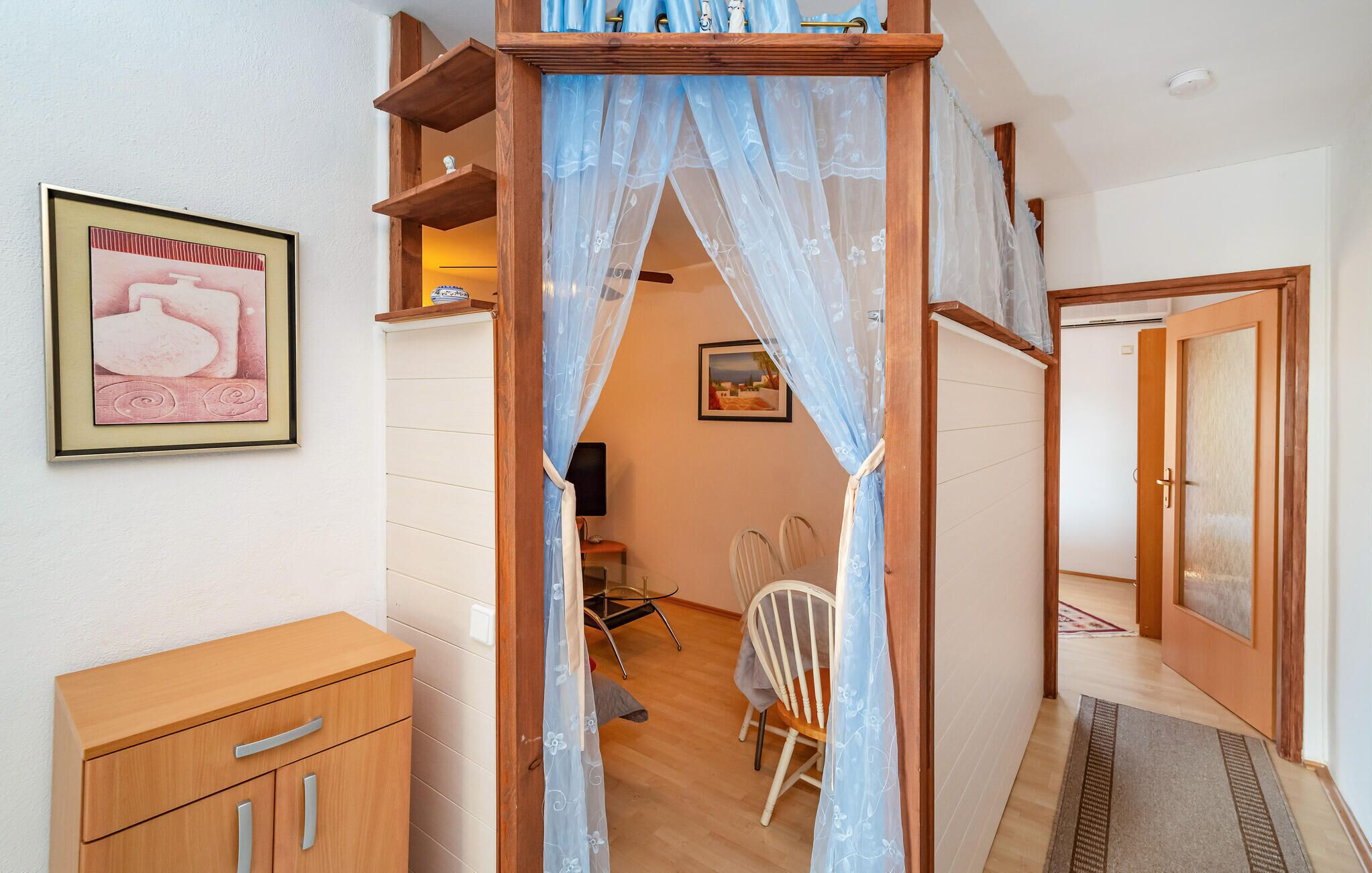 A room with a wooden wardrobe, a chair, a desk, and a bed with a canopy.
