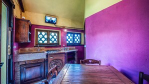 A room with a wooden table, two windows with decorative grills, a wooden cabinet, and a television mounted on the wall.