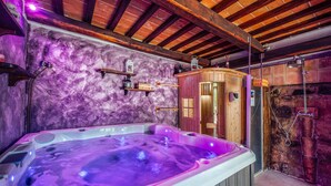 A spa area with a hot tub, wooden shelves, a wooden sauna, and a stone wall.