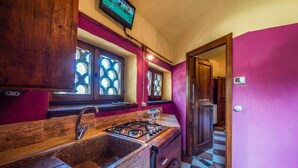 A kitchen with a gas stove, a sink, and wooden cabinets. There is a window with a decorative glass pattern and a television mounted above it.