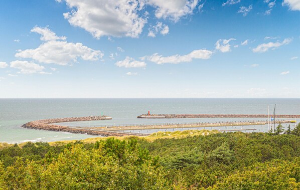 Un paisaje costero con un rompeolas curvo, un faro y abundante vegetación en primer plano.
