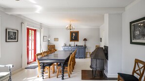 Uma sala de jantar com uma mesa comprida, cadeiras, um lustre e quadros nas paredes.