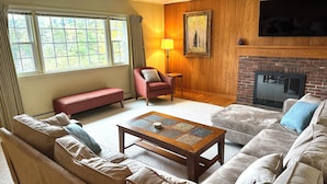A living room with a fireplace, a sofa, a red armchair, and a wooden coffee table. - Pet-friendly Rustic Mtn House (Woodstock)