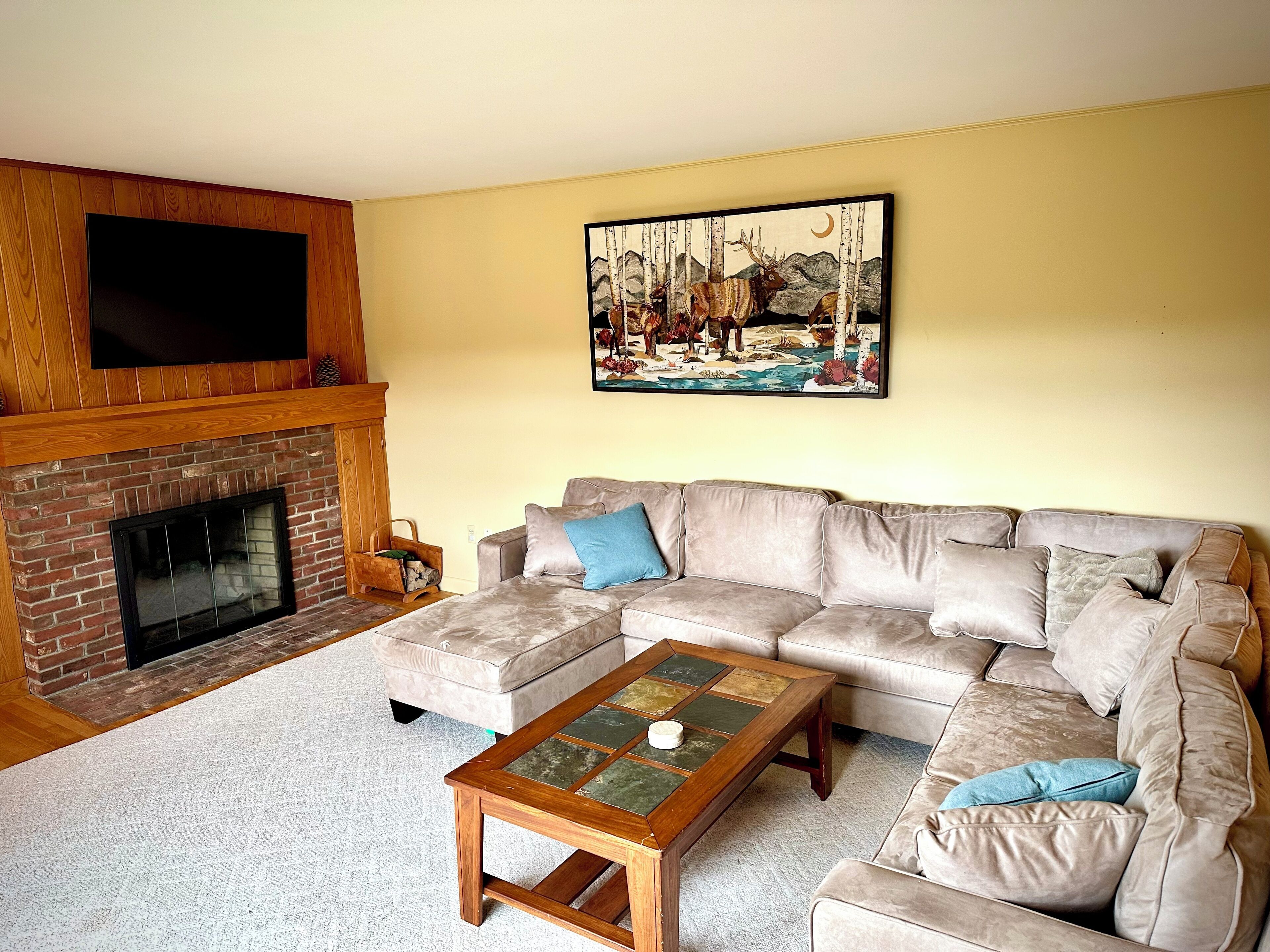 A living room with a fireplace, a large sofa, a coffee table, and a painting on the wall.