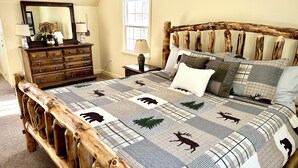 A bedroom with a wooden bed frame, a quilt with animal prints, a dresser, and a mirror. - Pet-friendly Rustic Mtn House (Woodstock)