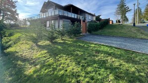 A modern two-story house with a balcony, surrounded by a well-maintained lawn and trees. - Ridge View Suite Seascape Panorama with Covered Deck  (Campbell River)