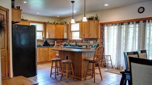 A kitchen with wooden cabinets, a black refrigerator, a central island with stools, and a dining area with chairs.